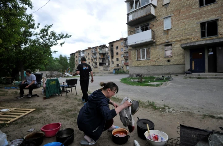 Une femme ukrainienne prépare à manger dans la rue, devant son immeuble bombardé et privé d'électrivité et de gaz, dans la petite ville de Moshchun, près de Kiev, le 27 mai 2022
