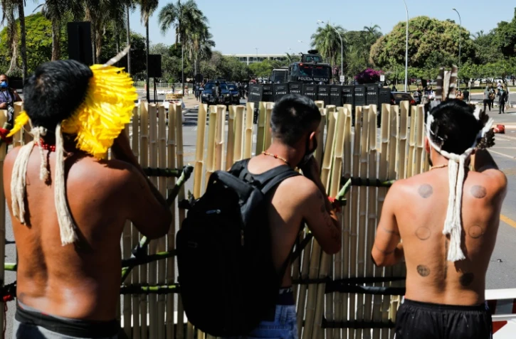 Des indigènes s'abritent derrière une palissade de bambou, face à des policiers, lors d'une manifestation devant le Parlement brésilien à Brasilia, le 22 juin 2021