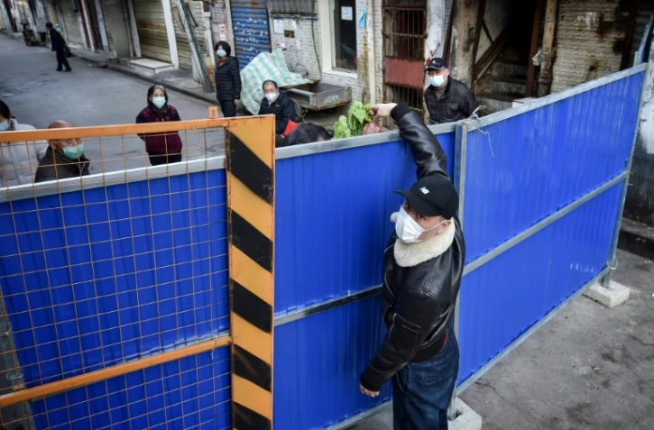 Un homme livre des légumes à une personne derrière une barrière à Wuhan le 24 février 2020
