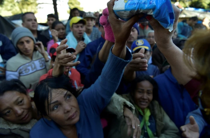 Des Vénézuéliens, installés dans un campement de fortune près d'une gare de bus, reçoivent un peu de nourriture, le 9 août 2018 à Quito, en Equateur