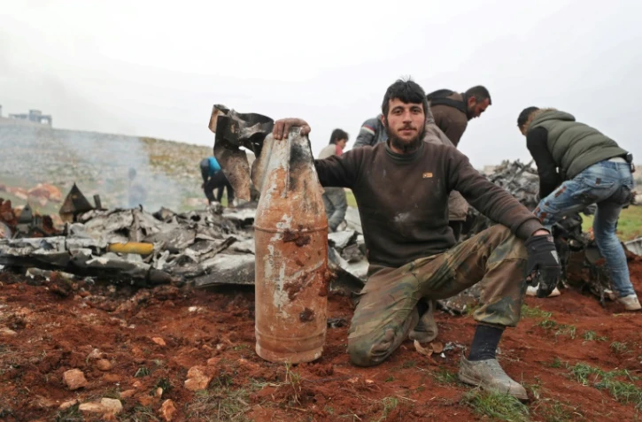 Un rebelle syrien pose avec un débris d'un hélicoptère de l'armée syrienne abattu, dans la province d'Alep (Syrie), le 14 février 2020