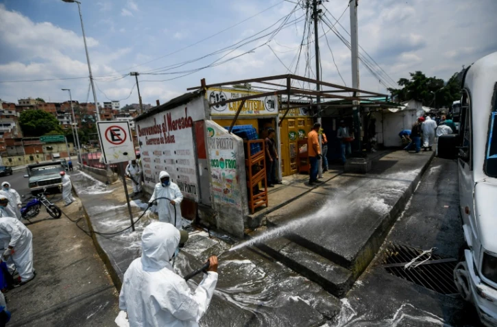 Des employés municipaux en combinaison de protection contre le coronavirus nettoient les rues de Petare, un quartier de Caracas, le 2 avril 2020 au Venezuela