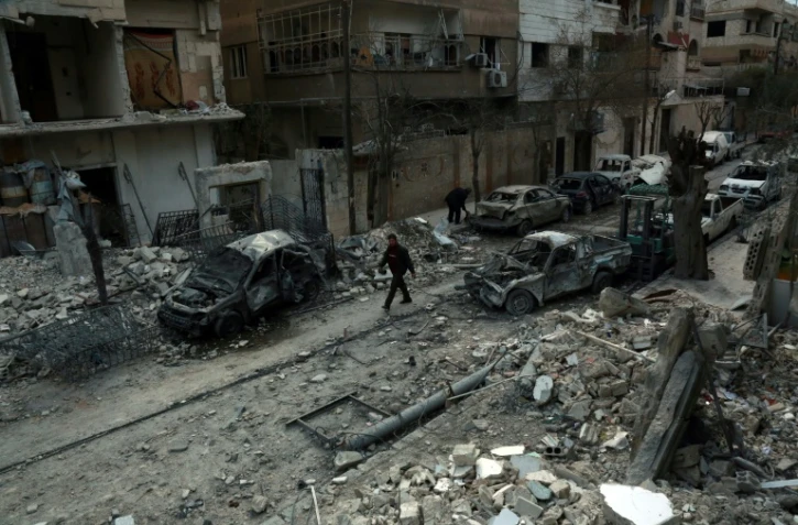 Photo prise le 25 février 2018 montrant un homme marchant dans une rue de la ville de Douma au milieu de voitures détruites et immeubles endommagés après des raids aériens du régime syrien sur la Ghouta orientale, une enclave rebelle près de Damas bombardée par le régime syrien