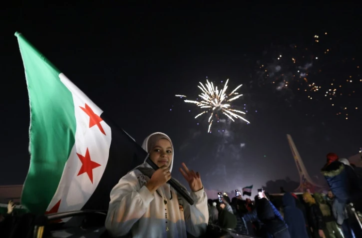 Une jeune femme tient le drapeau de la Syrie devant une foule célèbrant le Nouvel An près de la place des Omeyyades à Damas, en Syrie, le 1er janvier 2025