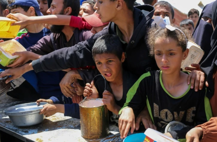 Des enfants palestiniens font la queue pour obtenir un repas chaud lors d'une distribution assurée par une cuisine soldiaire au camp de réfugiés de Nousseriat, dans le centre de la bande de Gaza, le 5 mai 2025