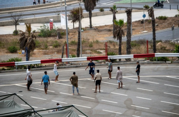 Des migrants jouent au foot sur un parking près d'abris temporaires installés pour eux, le 27 août 2026 à Ceuta