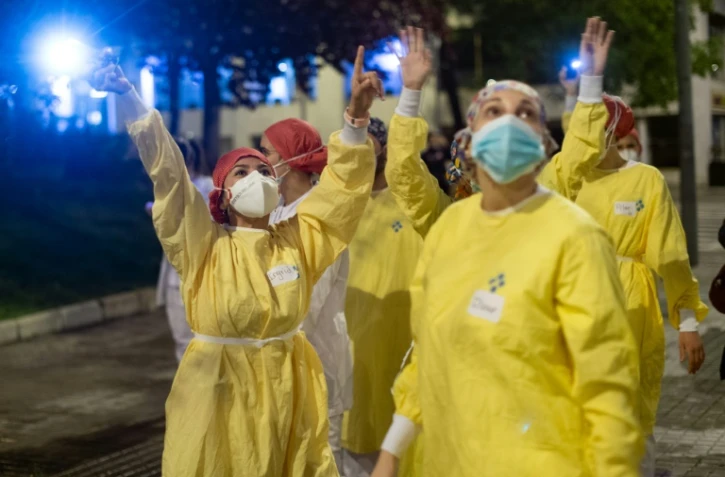 Des personnels soignants saluent les personnes qui les applaudissent devant l'Hôpital de Barcelone, le 13 avril 2020 en Espagne