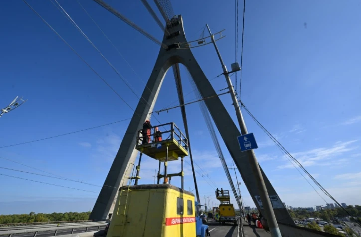 Des techniciens réparent une ligne électrique de trolleybus à proximité des dégâts constatés sur un pilier du pont, à la suite d’une attaque de drone contre le pont du Nord à Kiev, le 3 octobre 2026