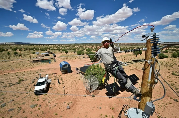 Cole Garcia, ouvrier de l'entreprise Mohave Electric, travaille sur un poteau électrique pour raccorder les maisons d'Amérindiens Navajo à Tonalea, en Arizona, le 8 juillet 2025