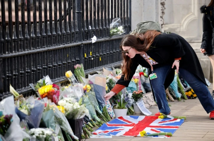 Une femme dépose un bouquet de fleurs en hommage au prince Philip devant les grilles du palais de Buckingham, à Londres, le 9 avril 2021.