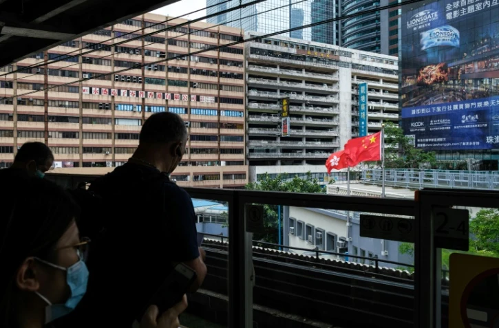 Des voyageurs sur le quai d'une station de métro à Hong Kong, avec le drapeau chinois en arrière-plan, le 29 mai 2020