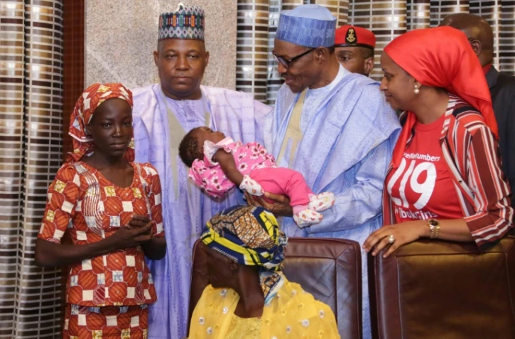 Le président du Nigeria Mohammadu Buhari (c) tient dans ses bras l'enfant d'Amina Ali (g), la première des 219 lycéennes de Chibok kidnappées par Boko Haram à avoir été retrouvée, le 19 mai 2016 à Maiduguri