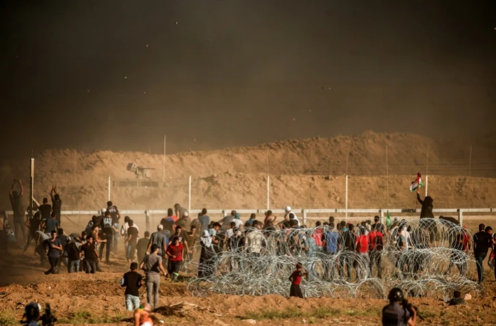 Des Palestiniens jettent des pierres aux soldats israéliens massés de l'autre côté de la frontière entre Israël et la bande de Gaza, le 27 juillet 2018