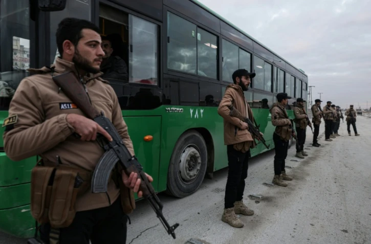 Des membres des forces gouvernementales syriennes surveillent un autobus transportant des combattants kurdes, le 10 janvier 2026 à Alep