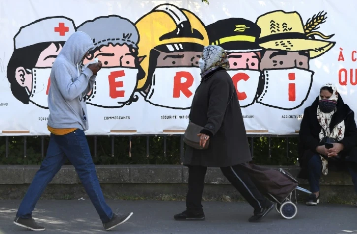 Des personnes passent devant une banderole remerciant le personnel soignant, les commerçants, la sécurité nationale les éboueurs, les postiers et les agriculteurs, à Paris, le 14 avril 2020