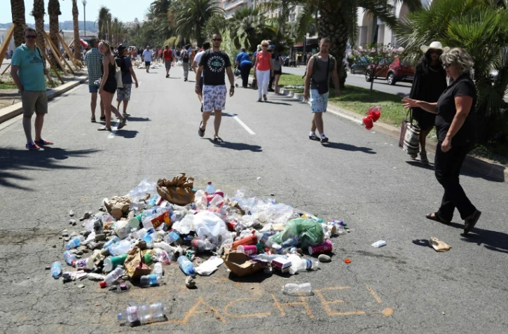 Des passants jettent le 18 juillet 2016 des détritus à l'endroit où aurait été tué Mohamed Des passants jettent le 18 juillet 2016 des détritus à l'endroit où a été tué Mohamed Lahouaiej-Bouhlel, près de l'inscription "Lâche!" sur le bitume