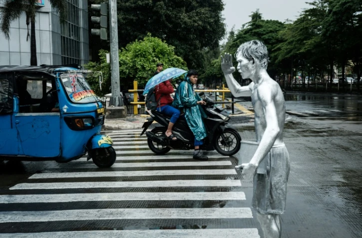 L'artiste de rue Ari Munandar (d), le corps recouvert de peinture argentée, fait la manche sous la pluie à un carrefour de Jakarta, le 1er avril 2025 en Indonésie