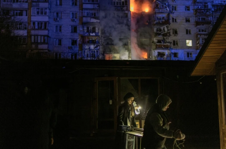 Des gens passent devant des magasins endommagés près d'un immeuble résidentiel en feu à la suite d'une attaque de drones russes sur la ville de Vychhorod, dans la banlieue de Kiev, tôt le matin du 30 novembre 2025