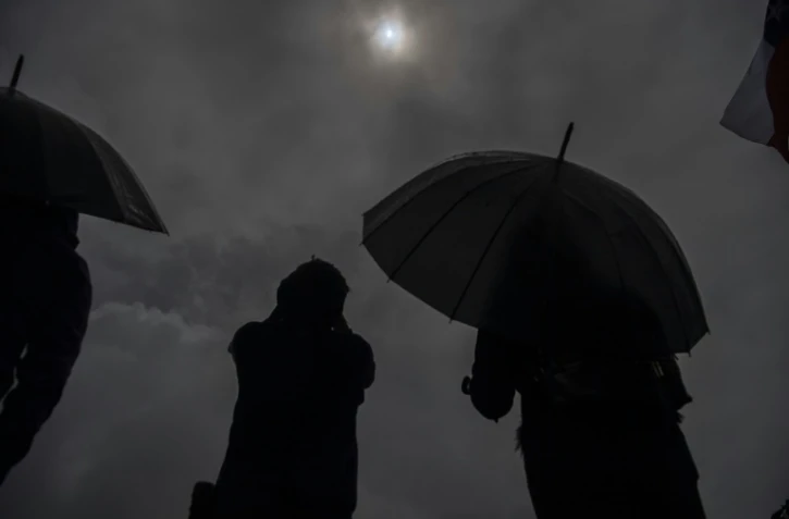 Des personnes observent sous la pluie l'éclipse solaire depuis les rives du lac Villarrica à Pucon, au sud du Chili, le 14 décembre 2020