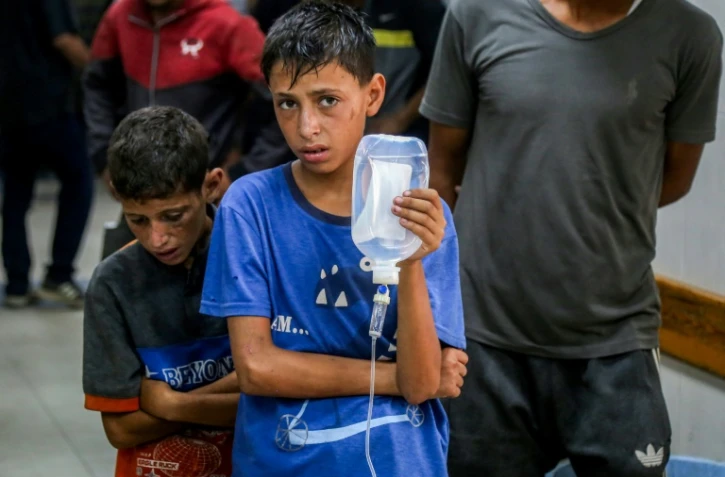 Un jeune palestinien tient une perfusion pour un homme blessé à l'hôpital Nasser, à Khan Younès, dans le sud de la bande de Gaza, le 20 juillet 2025