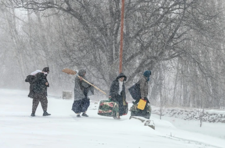 Des habitants marchent sous la neige avec leurs effets personnels sur une route de dans la province afghane de Parwan, dans l'est du pays, le 21 janvier 2026 