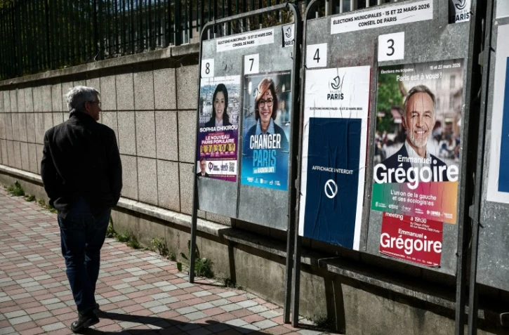 Une personne passe devant des affiches électorales pour les municipales, le 18 mars 2026 à Paris