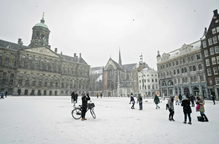 Des piétons traversent la place du Dam couverte de neige, le 7 février 2021 à Amsterdam
