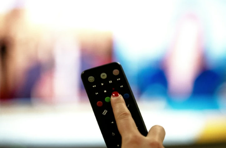 Une personne tient une télécommande pointée vers un écran de télévision, à Paris le 15 janvier 2025