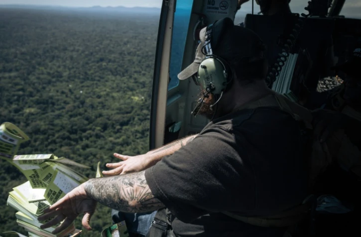 L'Américain Caleb Weiss, employé de la fondation américaine Bridgeway, lance des tracts depuis un hélicoptère sur les bastions des ADF, les exhortant à se rendre, le 8 mai 2024 au-dessus du territoire de Beni, dans la province du Nord-Kivu, dans l'est de la RDC
