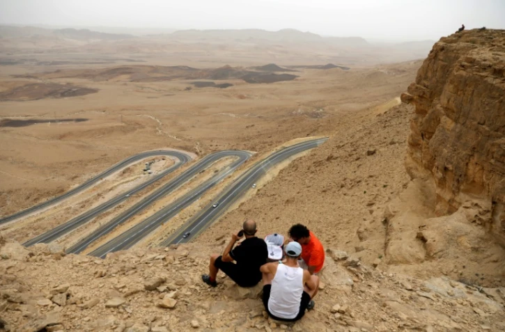 Des touristes assis au bord du "cratère" de Ramon, dans le désert du Néguev en Israël, le 6 mai 2018