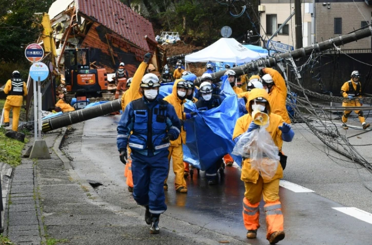 Des secouristes évacuent le corps d'une victime d'un glissement de terrain dans la ville d'Anamizu dans le département Ishikawa, le 6 janvier 2024, après le séisme du Nouvel An au Japon