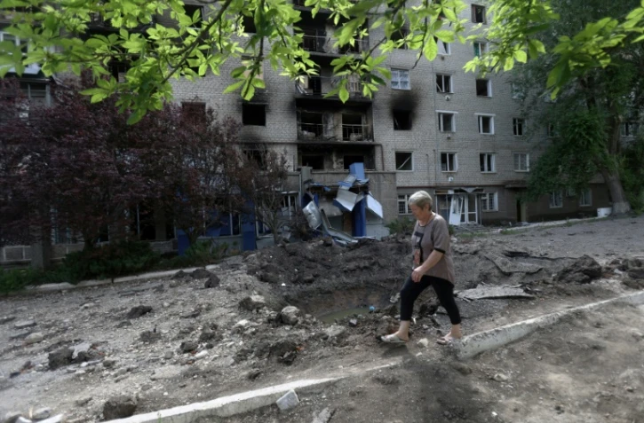 Une femme passe le long d'un cratère provoqué par un obus en face d'un immeuble résidentiel à Siversk, dans la région de Donetsk le 23 juin 2022