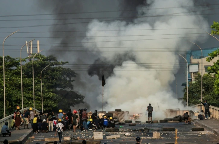 Des manifestants opposés au coup d'Etat militaire derrière une barricade lors de heurts avec les forces de police, le 16 mazrs 2021 à Rangoun, en Birmanie