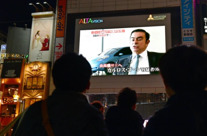 Des passants regardent le 22 novembre 2018 à Tokyo la photo de Carlos Ghosn, patron de Renault-Nissan, arrêté pour soupçons de malversations financières et fraude fiscale