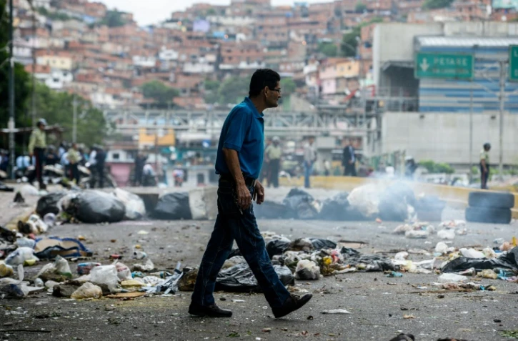 Un homme traverse une route barrée par des sacs poubelles, le 2 mai 2017 à Caracas