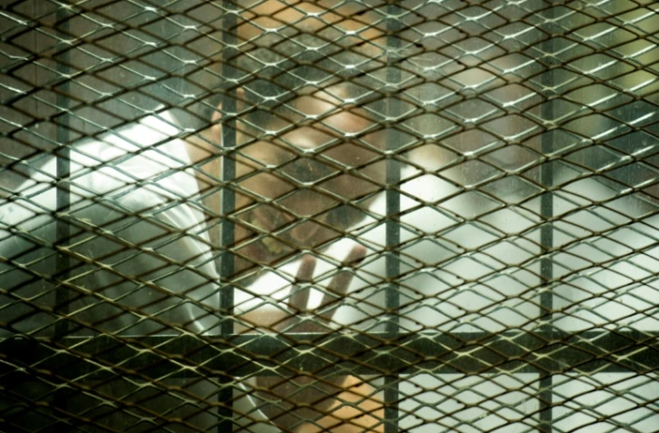 Le photojournaliste égyptien Mahmoud Abu Zeid "Shawkan" fait le V de la victoire dans le box des accusés devant les journalistes au tribubal au Caire le 8 septembre 2018