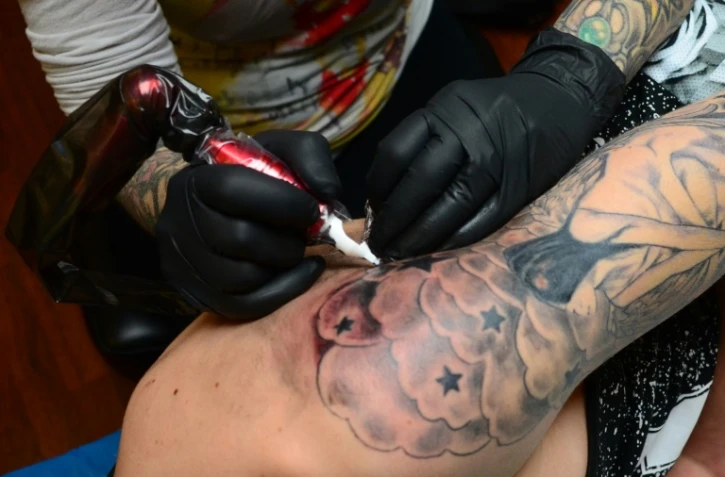 La tatoueuse Corinne Dubosque (L) travaille sur le bras de Timothée, 18 ans, dans son atelier Paradise Tattoo à Plessis Trevise dans la banlieue de Paris, le 9 février 2016