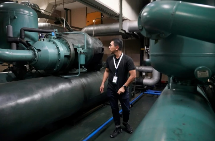 Un technicien de la société Recoolit travaille à capturer les gaz de refroidissemen d'une grande unité de climatisation au sous-sol d'un complexe d'habitation à Jakarta, le 10 juin 2025 en Indonésie 
