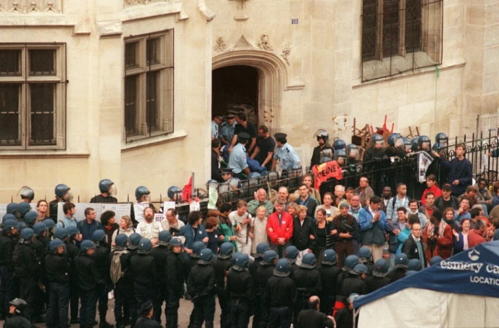 Un gréviste de la faim est sorti sur un brancard de l'église Saint-Bernard, alors qu'un groupe de sympathisants des sans-papiers est encadré par les forces de l'ordre, le 23 août 1996 à Paris