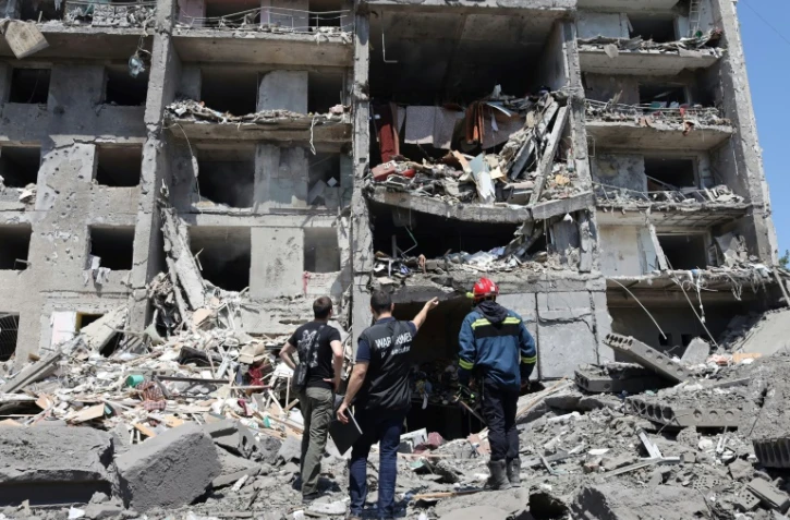 Un procureur pour crimes de guerre, un sauveteur et un civil, près d'un bâtiment détruit après avoir été touché par une frappe de missile dans la ville ukrainienne de Serhiivka, près d'Odessa, tuant au moins 18 personnes et en blessant 30, le 1er juillet 2022