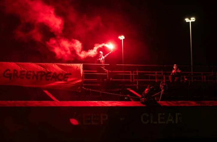 Un militant tient une fusée éclairante à côté d'une banderole "Greenpeace", lors d'une opération visant à bloquer le cargo Mikhail Dudin à Dunkerque, le 2 mars 2026 dans le Nord