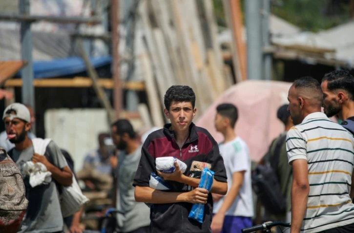 Des déplacés palestiniens portent des produits alimentaires obtenus à un point de distribution du centre de la bande de Gaza, le 26 juillet 2025