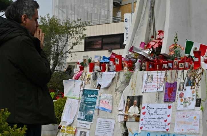 Un homme prie devant la statue de Jean-Paul II à l'extérieur de l'hôpital Gemelli à Rome où le pape François est soigné pour une pneumonie, le 8 mars 2025