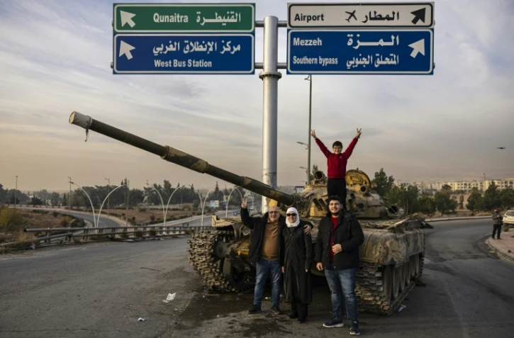 Des Syriens posent devant un tank détruit à Damas, après la prise de la capitale par les rebelles, le 12 décembre 2024