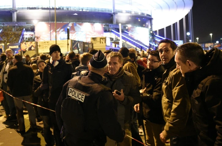 Un policier devant un cordon de sécurité derrière lequel des supporteurs de l'équipe de France de foot attendent après une série d'explosions au Stade de France, le 13 novembre 2015 à Saint-Denis, près de Paris