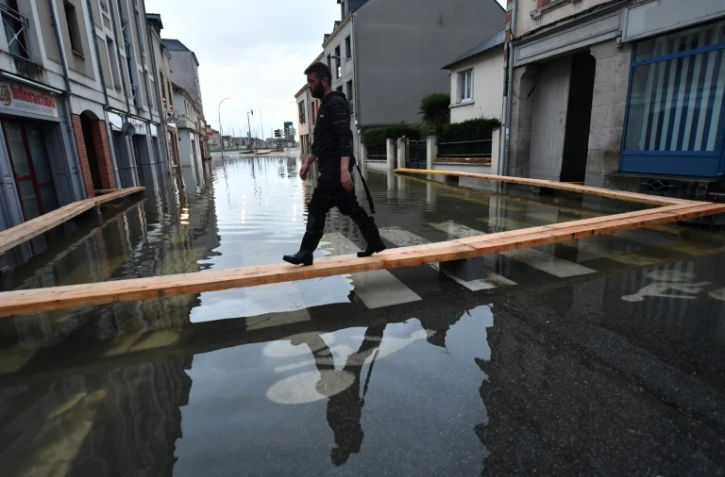 Un homme marche sur des planches surélevées pour circuler dans une rue inondée de Redon, le 30 janvier 2025, en Ille-et-Vilaine