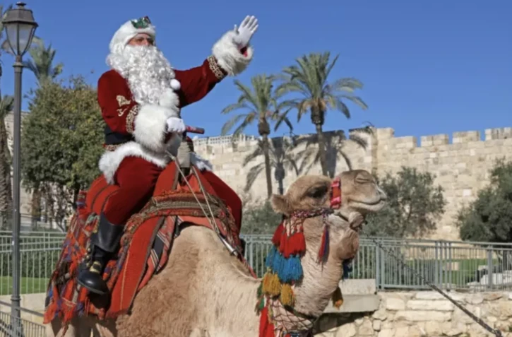 Le Palestinien Issa Kassissieh habillé en Père Noël pose pour une photo à dos d'un chameau dans la vieille ville de Jérusalem, le 2 décembre 2022 ( AFP / AHMAD GHARABLI )